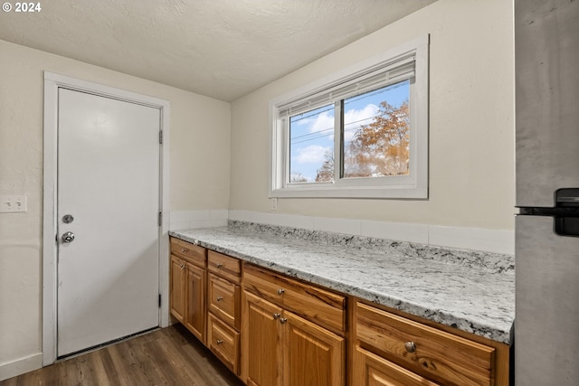 interior space featuring dark wood-type flooring, a textured ceiling, light stone counters, and stainless steel fridge