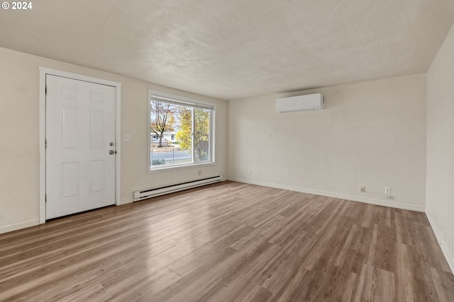 interior space with a textured ceiling, a wall mounted air conditioner, light hardwood / wood-style floors, and a baseboard heating unit