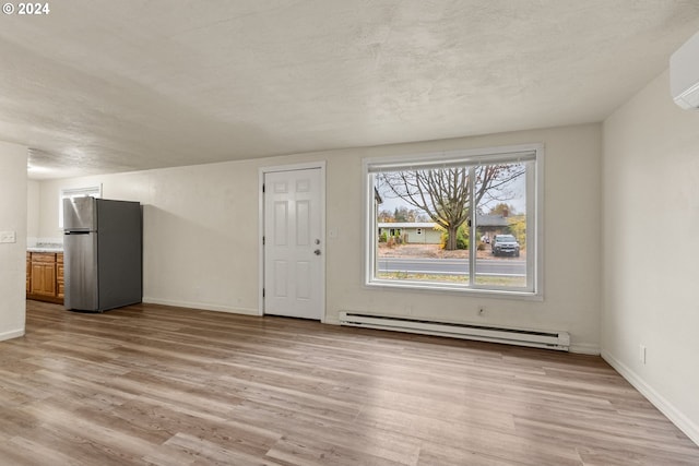 unfurnished living room featuring light hardwood / wood-style flooring, a textured ceiling, a wall mounted AC, and a baseboard heating unit