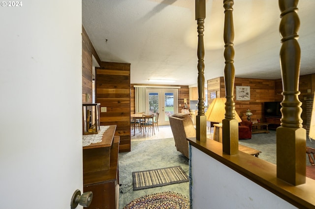 interior space featuring carpet flooring, french doors, a textured ceiling, and wooden walls