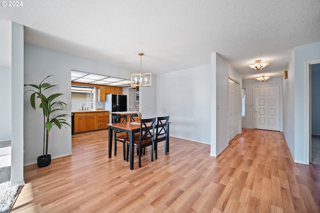 dining area with a chandelier, a textured ceiling, and light wood-type flooring