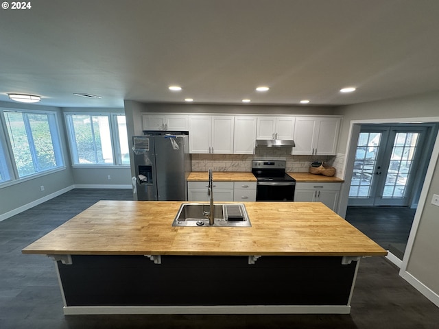 kitchen with appliances with stainless steel finishes, a kitchen island with sink, sink, white cabinets, and butcher block counters