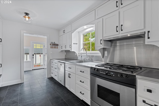 kitchen featuring dark tile patterned floors, stainless steel appliances, sink, white cabinetry, and tasteful backsplash