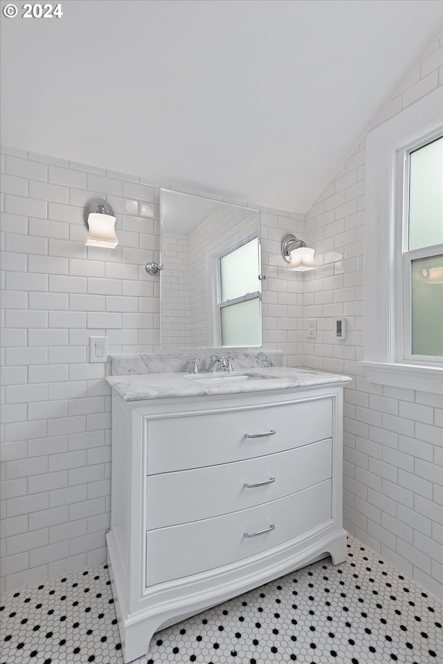 bathroom with tiled shower, lofted ceiling, tile patterned floors, vanity, and tile walls