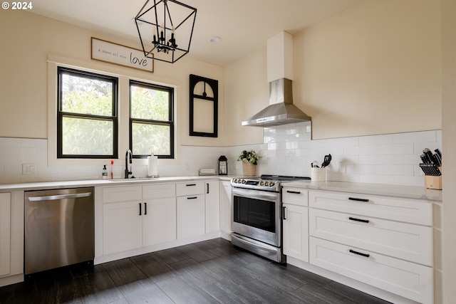 kitchen featuring pendant lighting, sink, wall chimney exhaust hood, white cabinetry, and stainless steel appliances