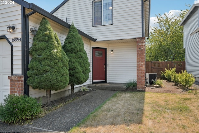 view of exterior entry with an attached garage, fence, and cooling unit