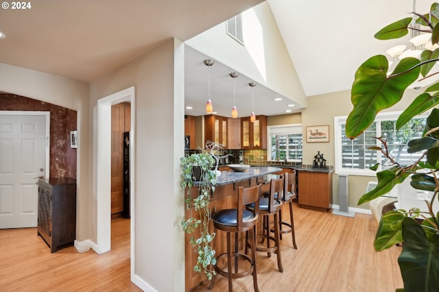 kitchen featuring pendant lighting, tasteful backsplash, light hardwood / wood-style flooring, a kitchen bar, and vaulted ceiling