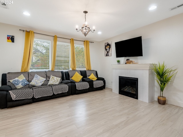 living room featuring light hardwood / wood-style floors, an inviting chandelier, and a tiled fireplace