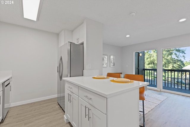 kitchen with white cabinets, a breakfast bar area, appliances with stainless steel finishes, and light hardwood / wood-style flooring