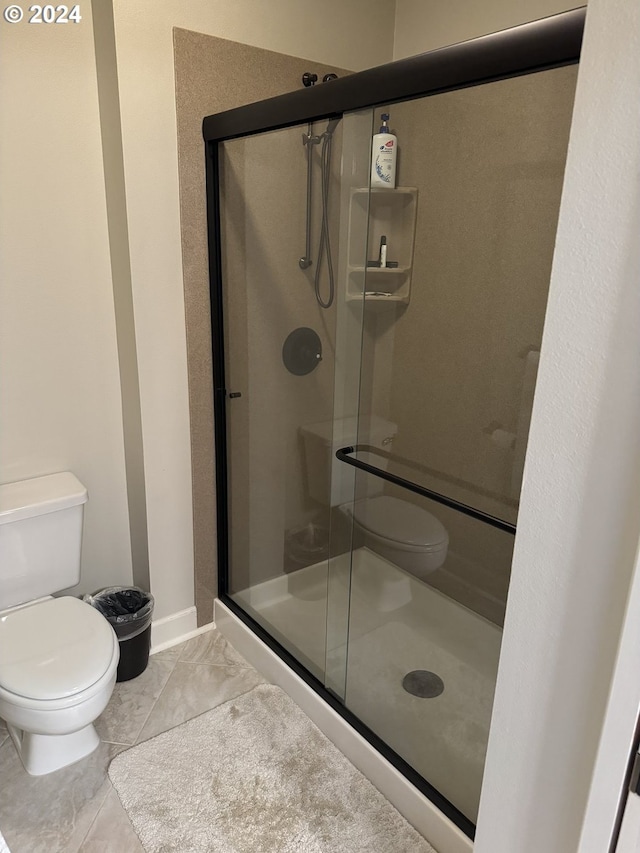 bathroom with tile patterned floors, toilet, and a shower with shower door