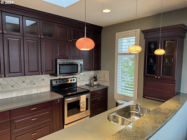 kitchen with light stone countertops, sink, tasteful backsplash, pendant lighting, and appliances with stainless steel finishes