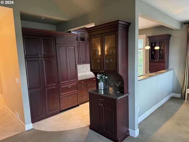 kitchen with tasteful backsplash, dark stone countertops, light colored carpet, and decorative light fixtures