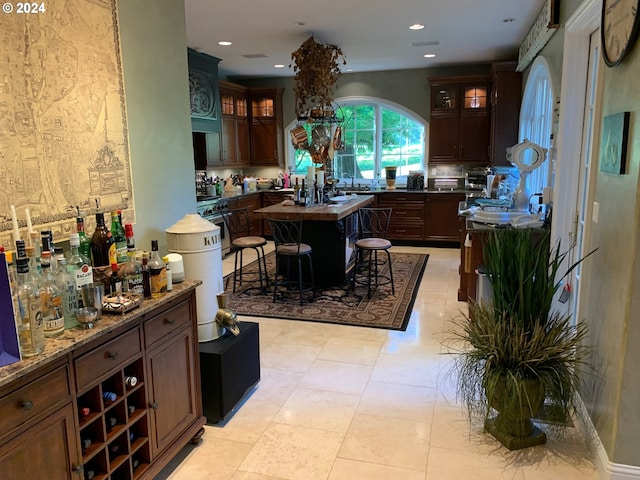 kitchen featuring dark brown cabinetry, a kitchen island, stainless steel stove, light tile patterned floors, and a breakfast bar area