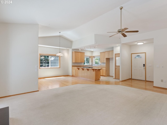 unfurnished living room with lofted ceiling, ceiling fan with notable chandelier, light hardwood / wood-style floors, and track lighting