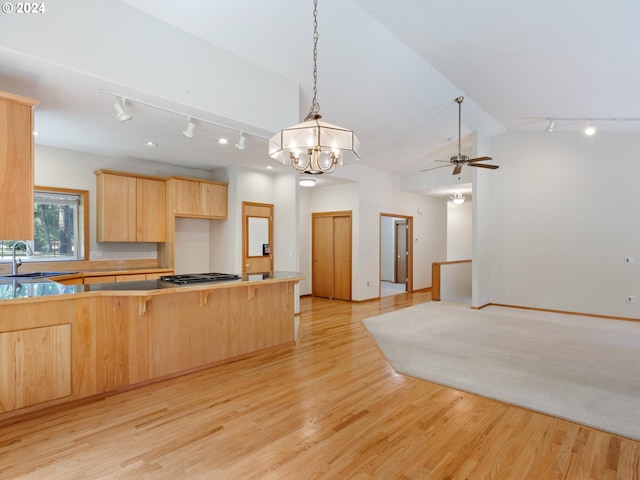 kitchen with ceiling fan with notable chandelier, a kitchen bar, light brown cabinetry, vaulted ceiling, and light hardwood / wood-style floors