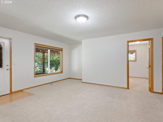 empty room with light colored carpet and a textured ceiling