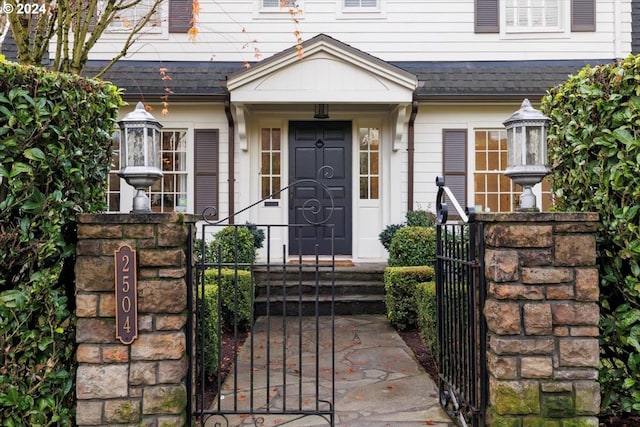 view of exterior entry featuring a shingled roof and a gate