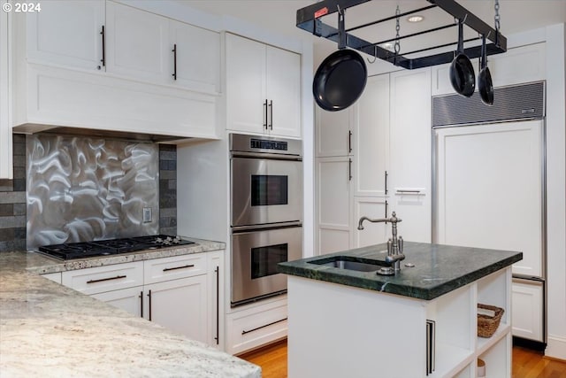 kitchen with white cabinets, paneled refrigerator, stainless steel double oven, and black gas cooktop