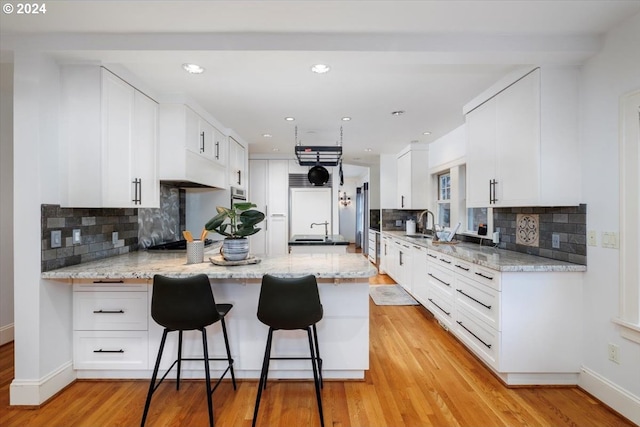 kitchen featuring kitchen peninsula, decorative backsplash, white cabinets, and light hardwood / wood-style floors