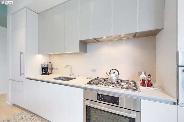 kitchen with white cabinetry, light hardwood / wood-style floors, appliances with stainless steel finishes, and sink