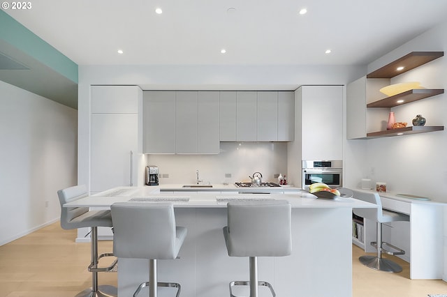 kitchen featuring sink, a kitchen bar, oven, gray cabinets, and light wood-type flooring