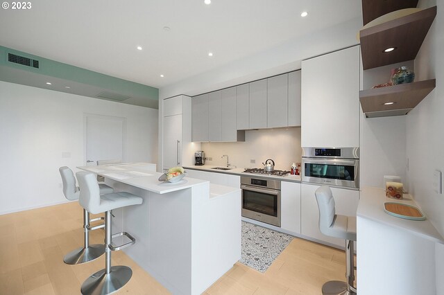 kitchen featuring white cabinetry, appliances with stainless steel finishes, a center island, and light hardwood / wood-style flooring