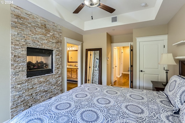 bedroom with hardwood / wood-style flooring, ceiling fan, a fireplace, connected bathroom, and a tray ceiling