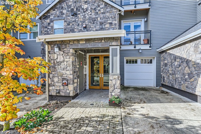 view of exterior entry with french doors, a balcony, and a garage