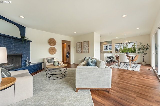 living room with an inviting chandelier, a brick fireplace, and hardwood / wood-style flooring