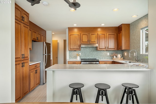 kitchen with sink, appliances with stainless steel finishes, a kitchen bar, decorative backsplash, and kitchen peninsula