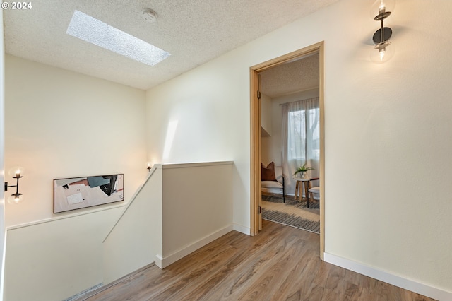 hall featuring a skylight, a textured ceiling, and light wood-type flooring