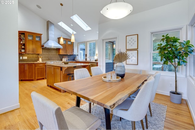 dining area with light hardwood / wood-style floors, high vaulted ceiling, and a skylight