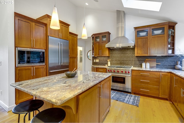 kitchen with a breakfast bar area, decorative backsplash, hanging light fixtures, wall chimney range hood, and built in appliances