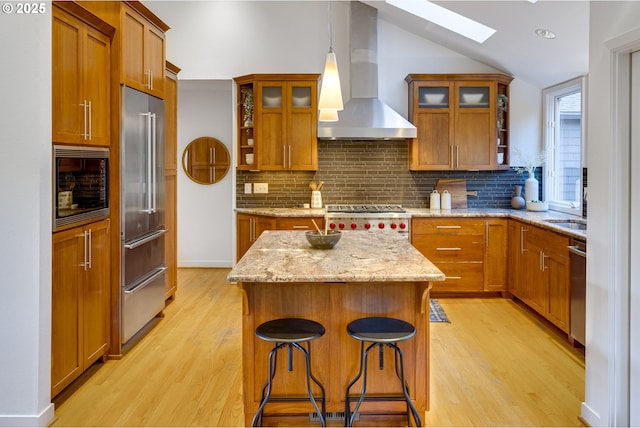 kitchen with pendant lighting, a center island, wall chimney exhaust hood, built in appliances, and light hardwood / wood-style floors