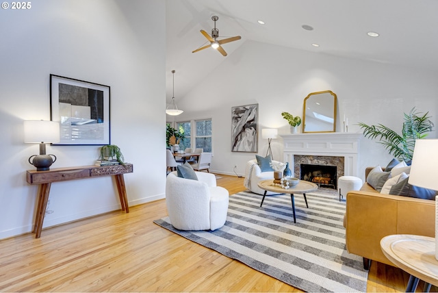 living room with high vaulted ceiling, ceiling fan, a fireplace, and light hardwood / wood-style flooring