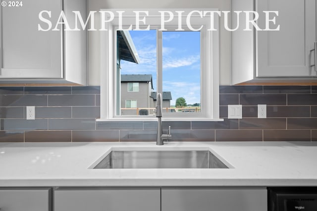 kitchen featuring white cabinetry, decorative backsplash, light stone countertops, and sink