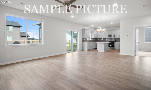 unfurnished living room featuring ceiling fan with notable chandelier and light wood-type flooring