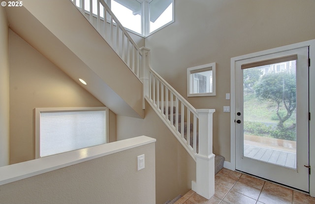foyer entrance with stairway, light tile patterned floors, baseboards, and a high ceiling