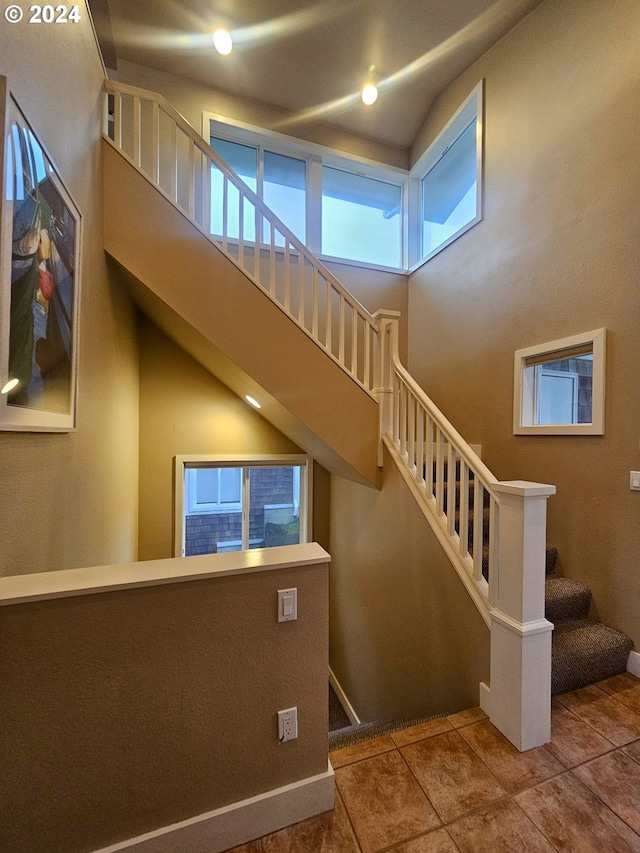 stairs featuring tile patterned floors, a high ceiling, and baseboards