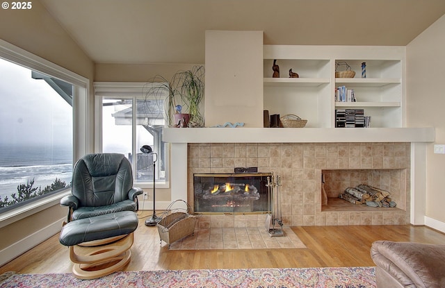 living area featuring wood finished floors, built in shelves, lofted ceiling, and a fireplace