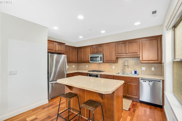 kitchen with a kitchen breakfast bar, sink, light hardwood / wood-style floors, appliances with stainless steel finishes, and a kitchen island