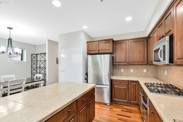 kitchen with decorative light fixtures, decorative backsplash, light wood-type flooring, tile counters, and stainless steel appliances