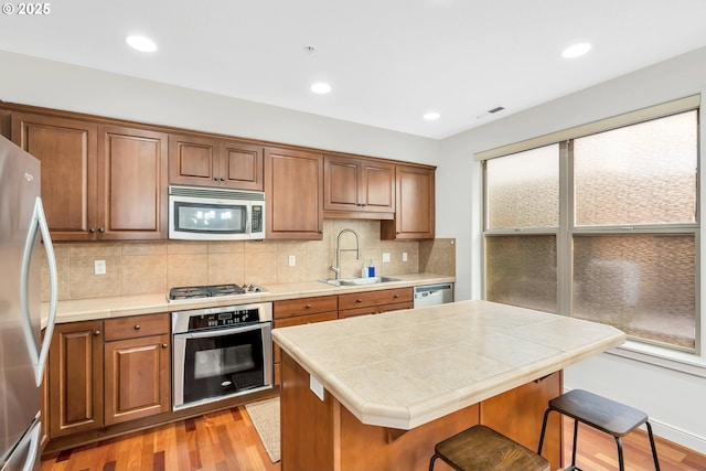 kitchen with appliances with stainless steel finishes, a breakfast bar, sink, a center island, and tile counters