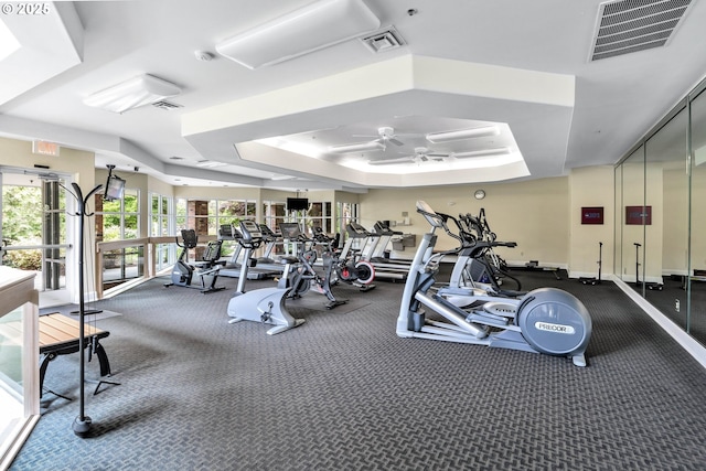 gym with a tray ceiling and ceiling fan