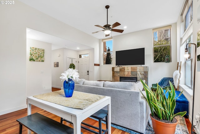 living room featuring wood-type flooring, ceiling fan, and a tiled fireplace