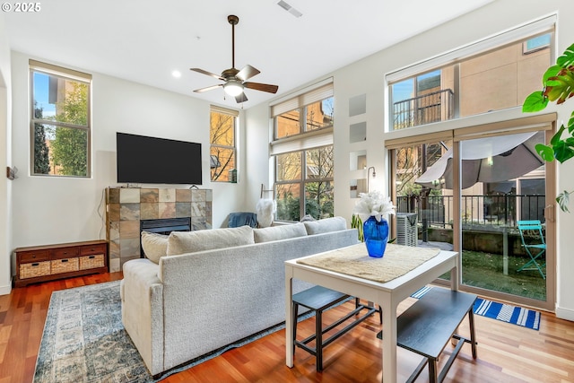 living room with hardwood / wood-style flooring, ceiling fan, a wealth of natural light, and a tiled fireplace