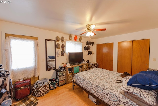 bedroom with light wood-type flooring, two closets, multiple windows, and ceiling fan