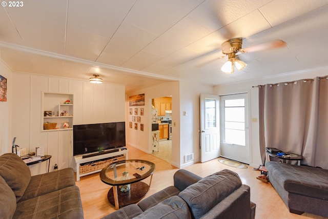 living room featuring built in shelves, ornamental molding, and ceiling fan