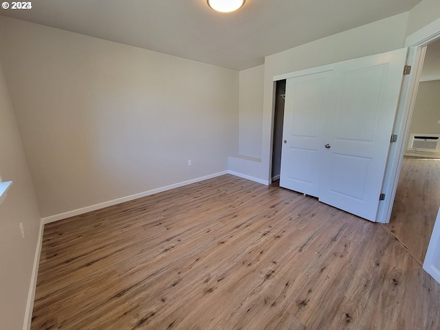 unfurnished bedroom featuring light hardwood / wood-style flooring, an AC wall unit, and a closet