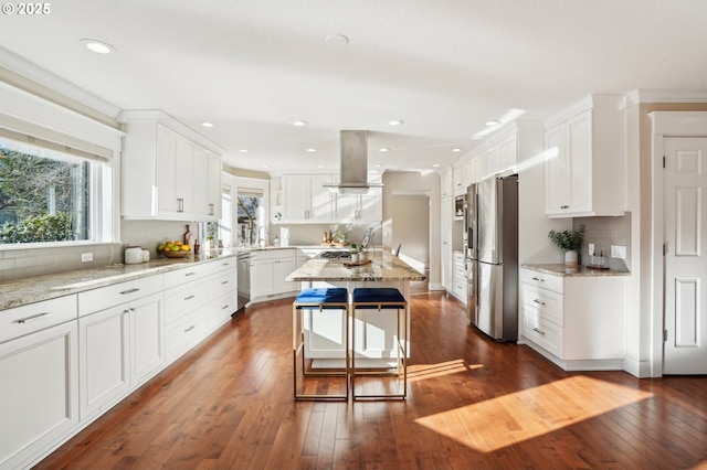 kitchen with light stone counters, island range hood, stainless steel appliances, and white cabinets